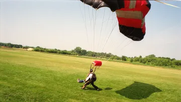 Fallschirmspringer landet auf offenem Rasenfeld.