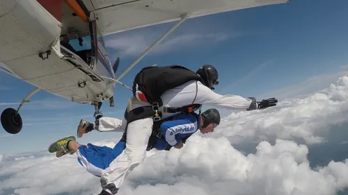 Two skydivers exit plane above clouds.