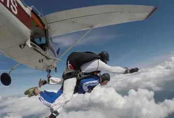 Zwei Fallschirmspringer springen aus Flugzeug über Wolken.