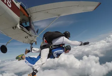 Zwei Fallschirmspringer springen aus Flugzeug über Wolken.