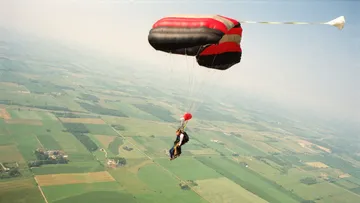 Fallschirmspringer mit Fallschirm über Feldern.