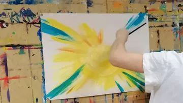 Person painting vibrant sun on canvas.