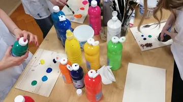 People painting with colorful bottles on table.