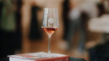 Wine glass with rosé on book indoors.