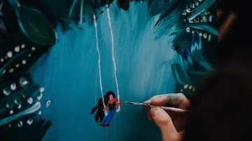 Hand painting person on swing, forest background.