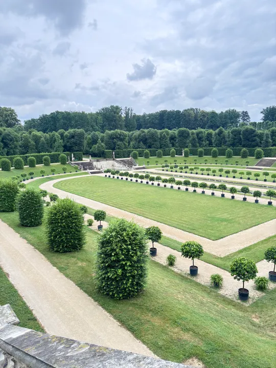 Gepflegter Garten mit Hecken unter wolkigem Himmel.
