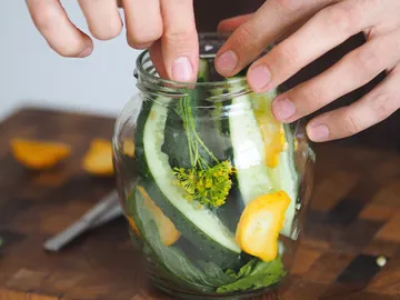 Ein Glas wird mit Gurken und Kräutern gefüllt.