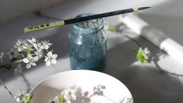 Pinsel auf Glas neben weißen Blumen.