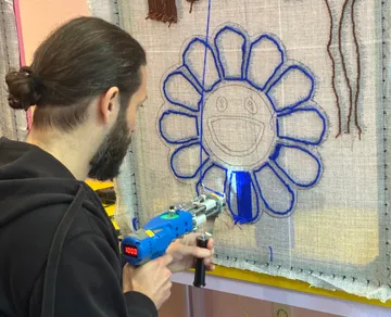Person tufting floral pattern on fabric.