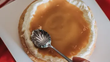 Spoon spreading caramel on cream-covered cake.