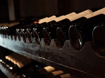 Wine bottles lie on a wooden rack in a dark environment.