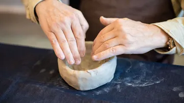 Hände formen Tonschüssel auf Tisch.