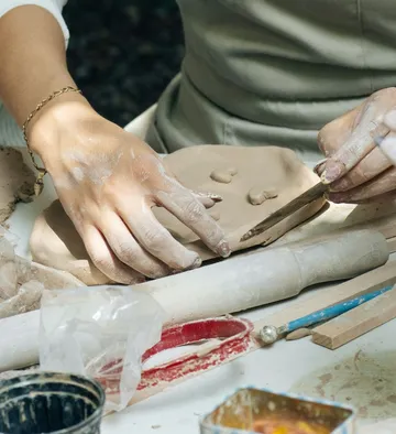 Hands sculpting clay in a workshop.