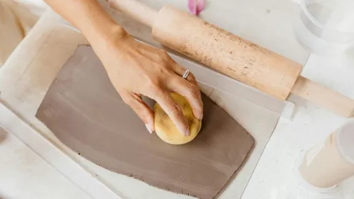Hand pressing clay with sponge, rolling pin nearby.