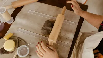 Hands rolling clay with rolling pin.