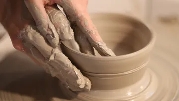 Hands shaping clay bowl on pottery wheel.
