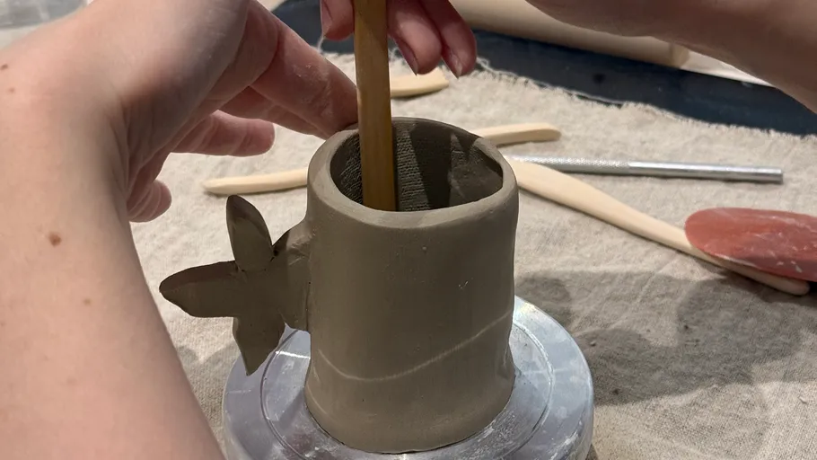 Hände formen Tonbecher mit Werkzeugen herum.