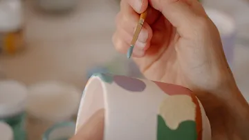 Hand painting colorful patterns on ceramic object.