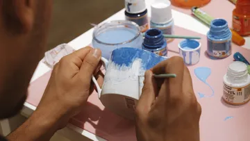 Person paints a mug with blue paint.