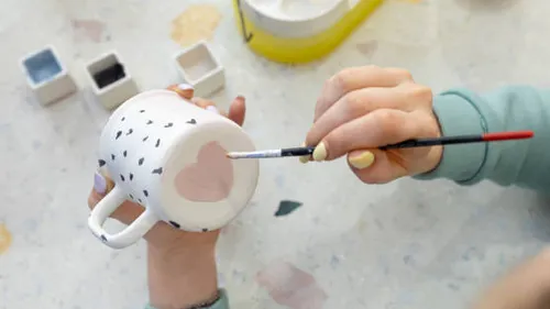 Person painting heart on ceramic mug.