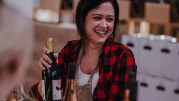 Woman holding wine bottle, smiling, indoors.