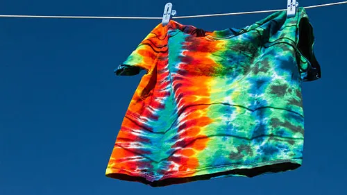 Tie-dye shirt hangs on clothesline outdoors.