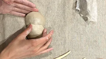 Hände formen Ton auf Leinwandoberfläche.