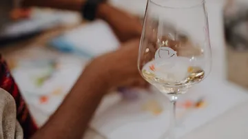 Wine glass on table with hands visible.