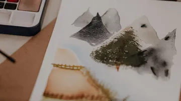 Watercolor mountains on paper beside paints.