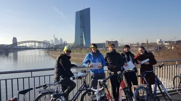 Gruppe mit Fahrrädern auf Brücke, Stadtsilhouette.