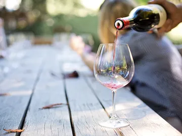 Rotwein wird in ein Glas auf einem Holztisch eingeschenkt.
