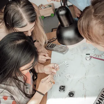 People crafting jewelry under a lamp.