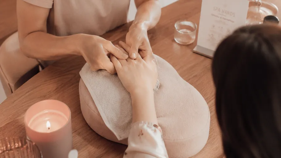 Hände massieren andere Hand in Spa-Umgebung.