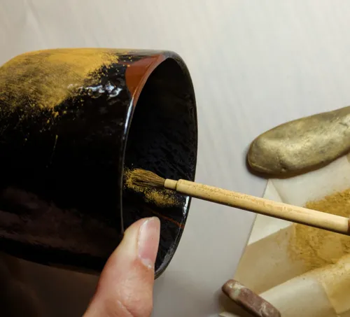 Hand painting black pottery with gold brush.