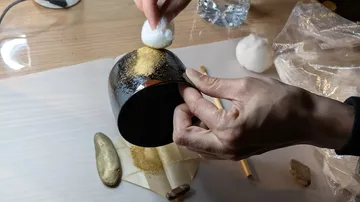 Hand trägt Goldstaub auf schwarzen Becher auf.