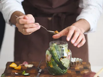 Ein Hand greift einen Löffel und fügt Zutaten in ein Glas.