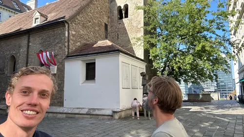Zwei Personen bei alter Steinkirche, sonniger Tag.