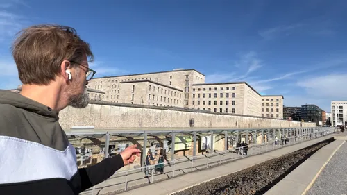 Mann zeigt auf historische Berliner Mauer im Freien.