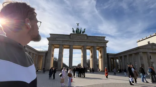 Man standing, observing Brandenburg Gate, sunny plaza.