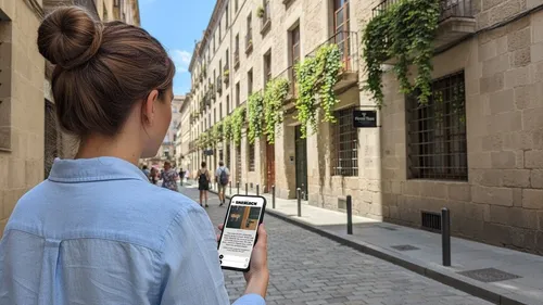 Woman checks phone walking on cobblestone street.
