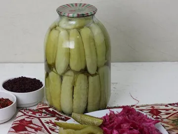 Glas mit eingelegten Gurken, umgeben von Gewürzen und Brot.