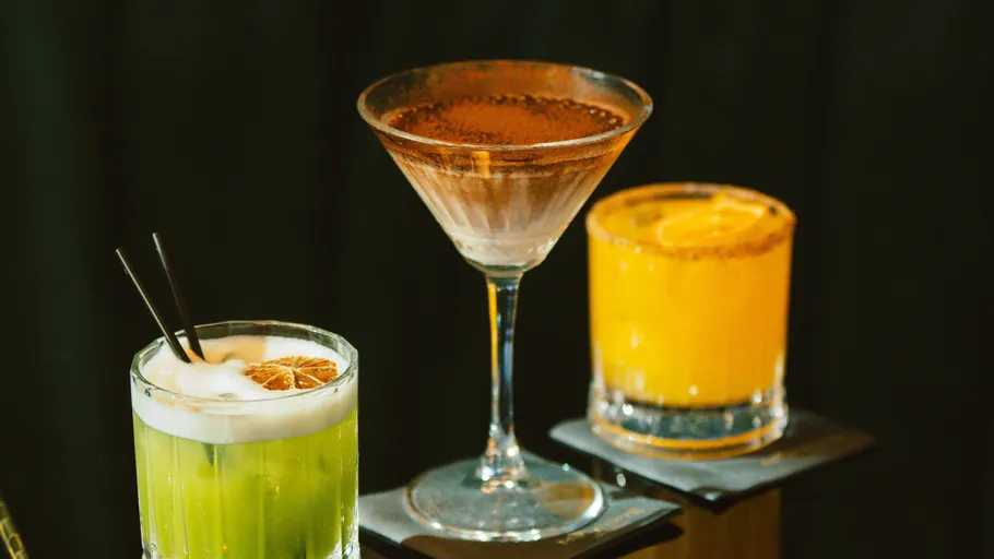Drei Cocktails auf Untersetzern bei schwachem Licht.