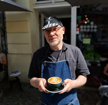 Mann hält Latte Art Tasse im Freien.