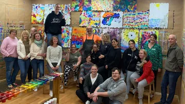 Gruppe posiert im Kunststudio mit Gemälden.