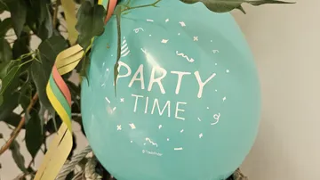 Ballon mit 'Party Time', umgeben von Blättern.