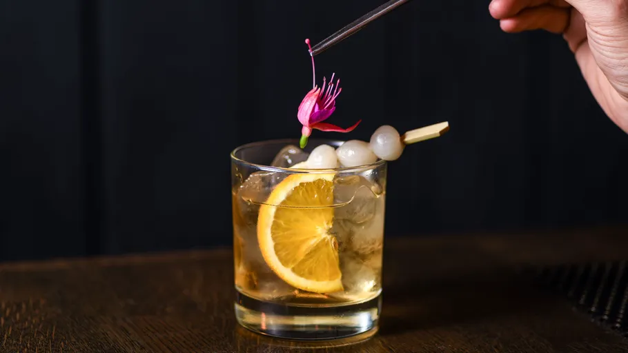 Glas mit Cocktail, Eis, Orangenscheibe, auf Tisch.