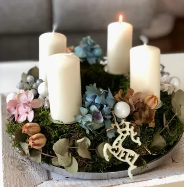 Vier Kerzen auf Blumenkranz, eine brennt.