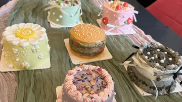 Sechs dekorierte Kuchen auf einem Stofftisch.