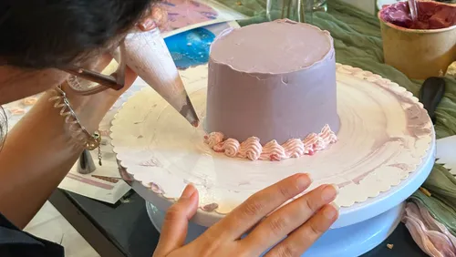 Person decorates purple cake on rotating stand.