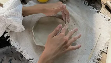 Hands shaping clay on a table.
